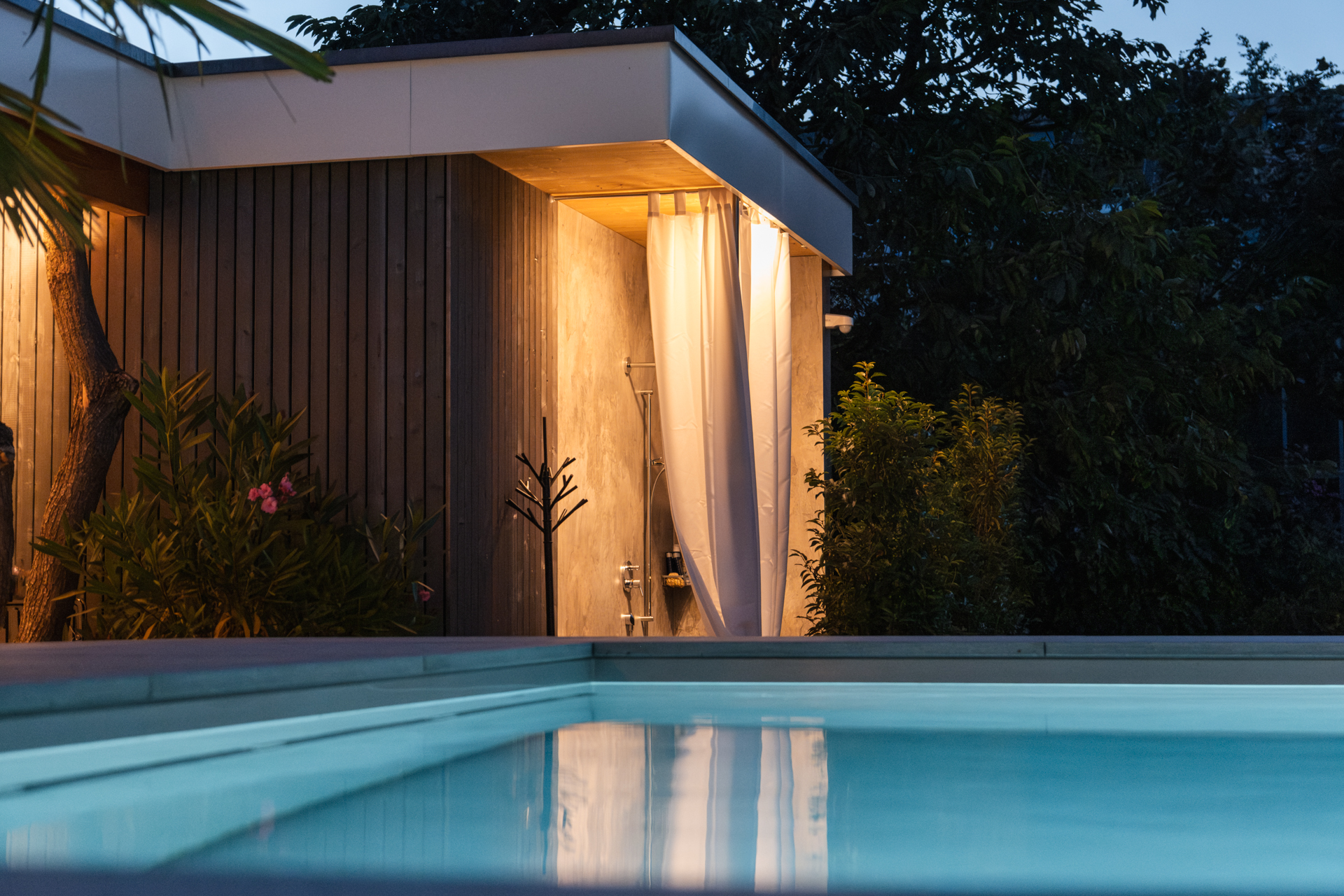 Outdoordusche im Hintergrund eines Swimminpools bei Nacht, mit Stimmungsvoller Beleuchtung. 