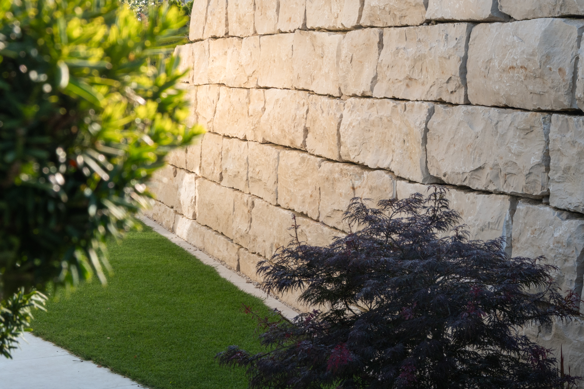 Rötlich Beige Sandsetinmauer im Detail mit Sträuchern im Vordergrund. 