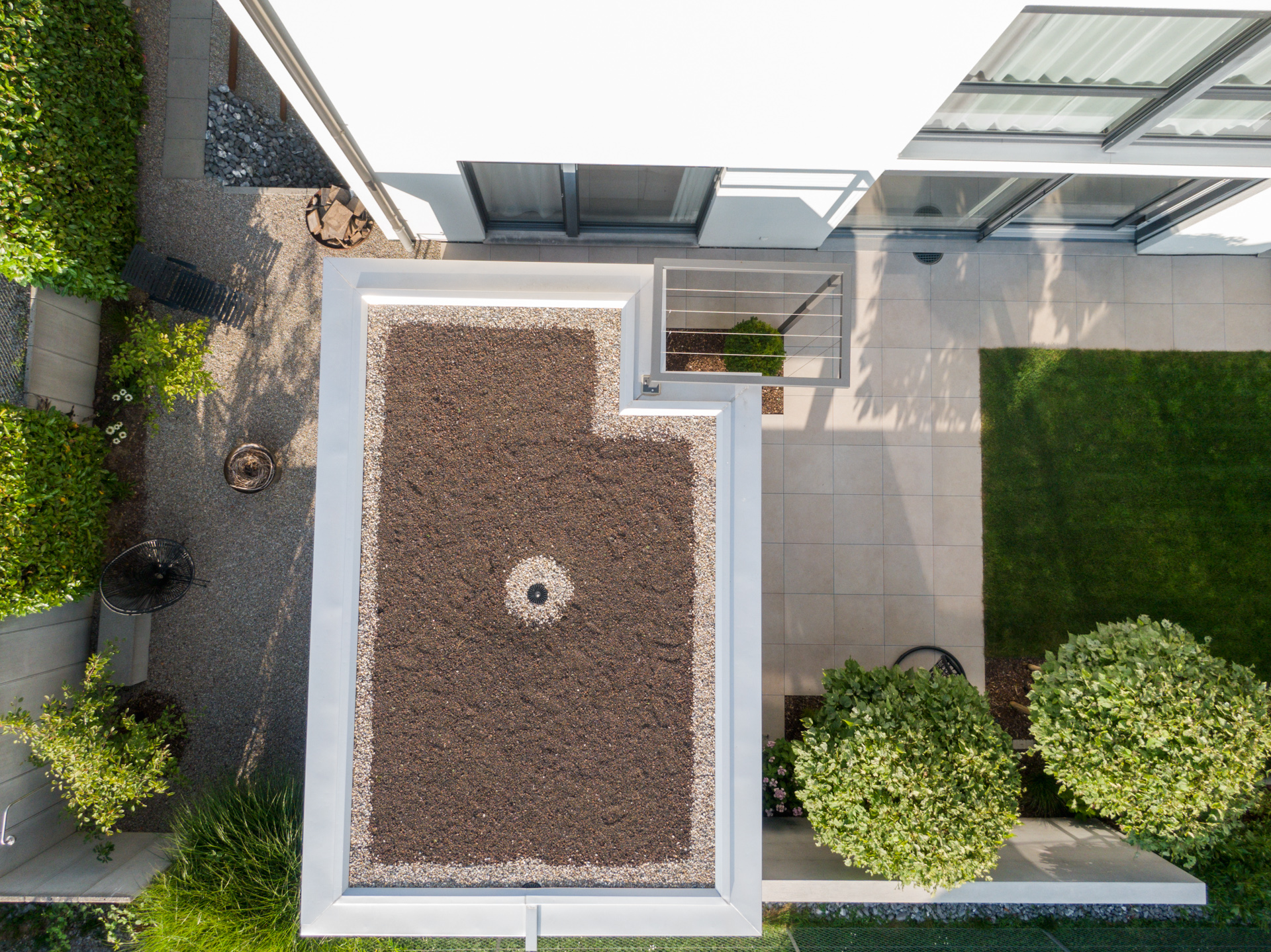 Vogelansicht eines Privatgartens mit Loggia, Kiesplatz, Wiesenfläche und Natursteinplatten. 