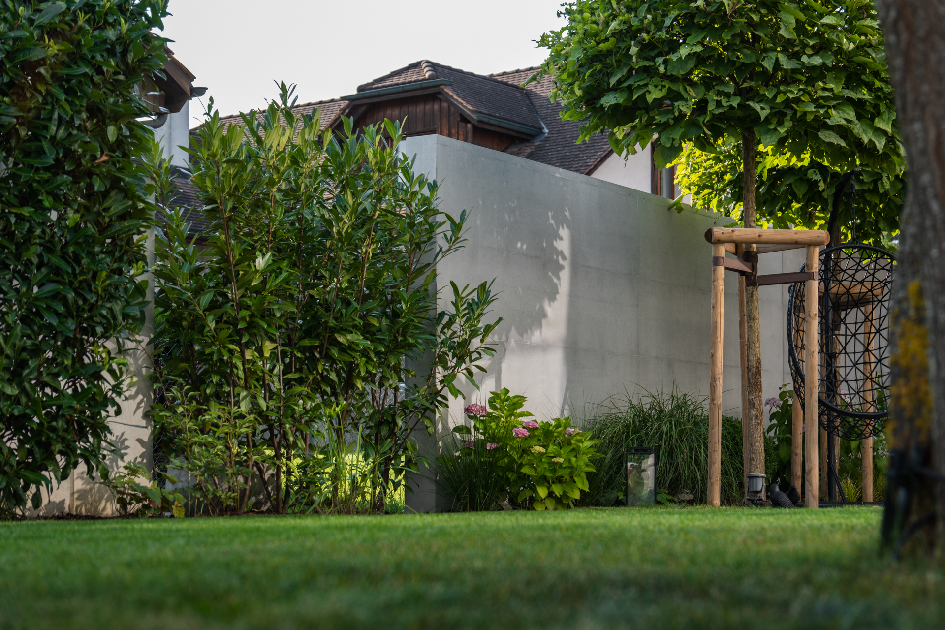 Beton Loggia von hinten mit schöner Bepflanzung und hochstämmigen Bäumen. 