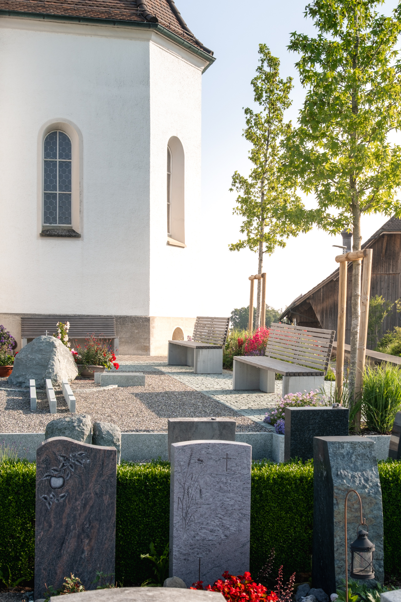 Kirche mit Grabsteinen und gemütlichen Sitzbänken bei Sonnenschein. 