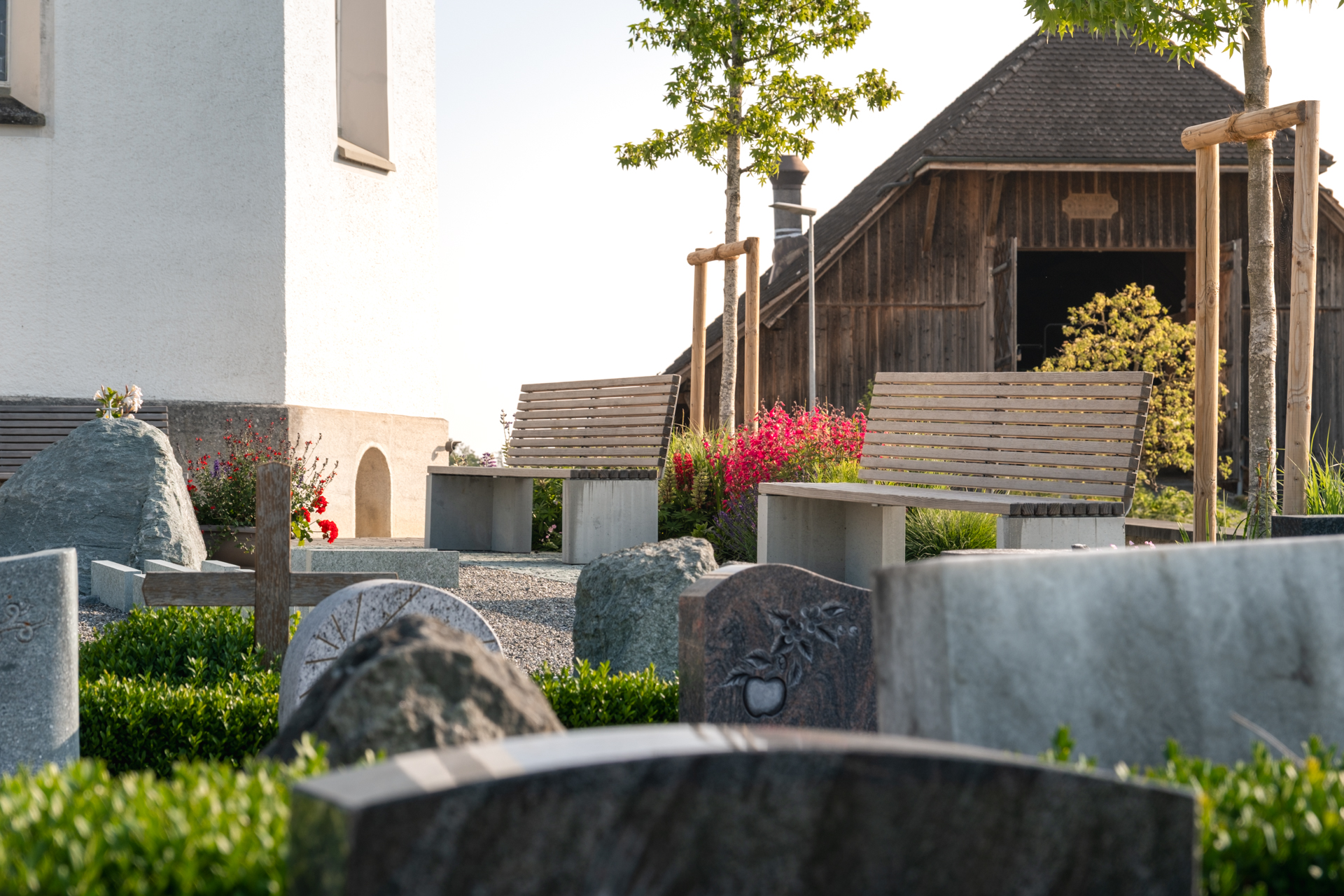 Kreuz und Grabsteine zwischen farbigen Blumenbeeten. 