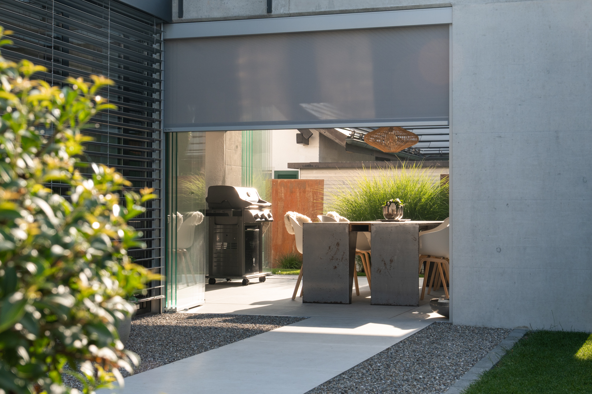 Wunderschön gestaltete Loggia mit Grill und hochwertigen Gartenmöbeln bei gleissendem Sonnenlicht. 