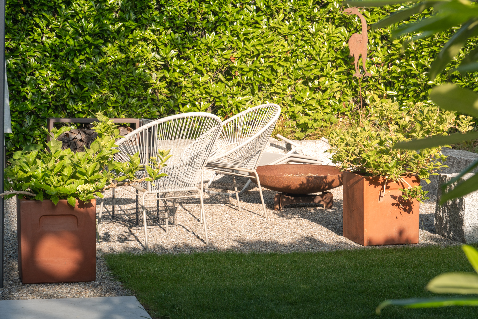 Rostrote Feuerschale in einem Gemütlichen Garten mit hochwertigen weissen Gartenmöbeln. 