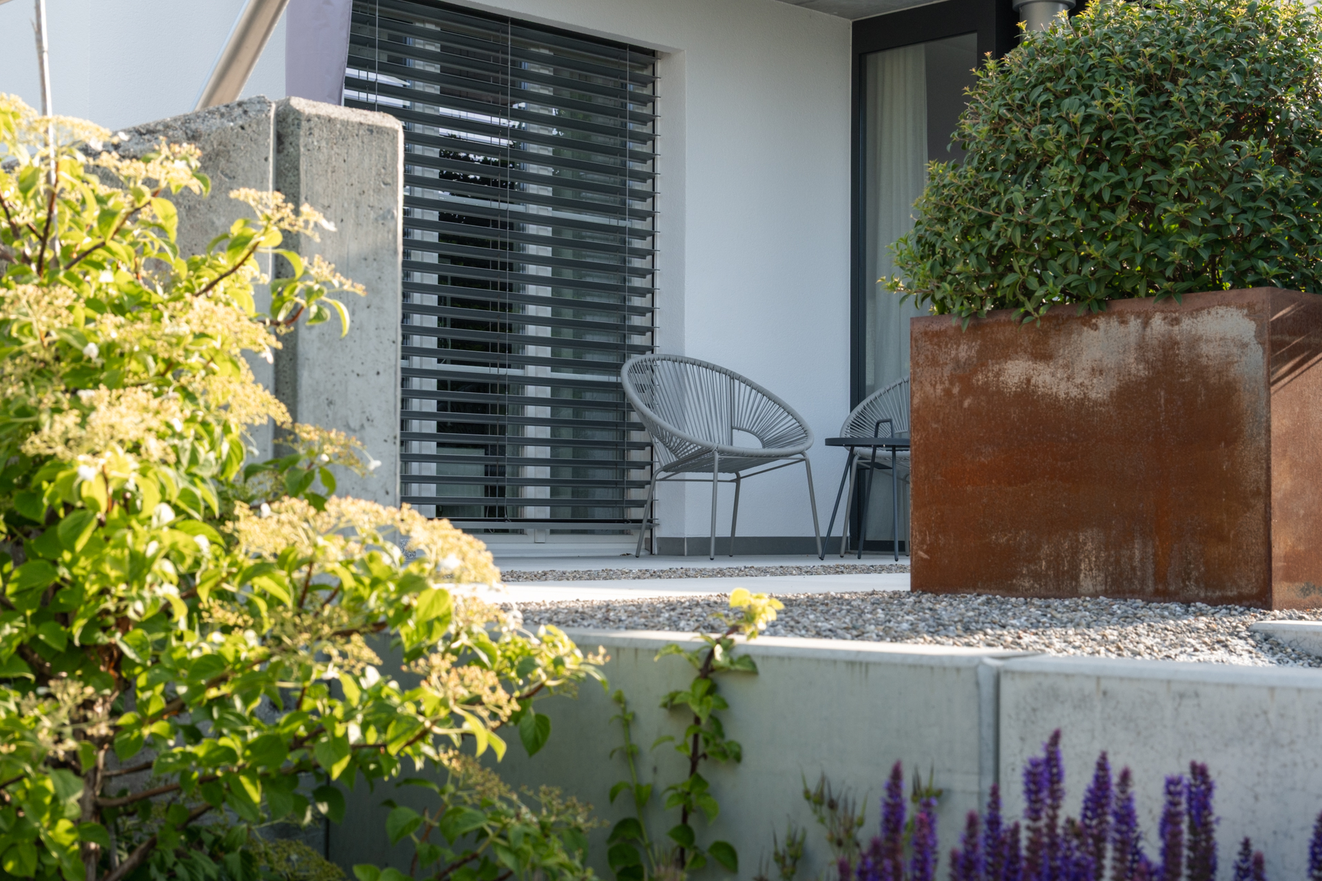 Stahlhochbeet in Kiesgarten mit buschigem Strauch. 