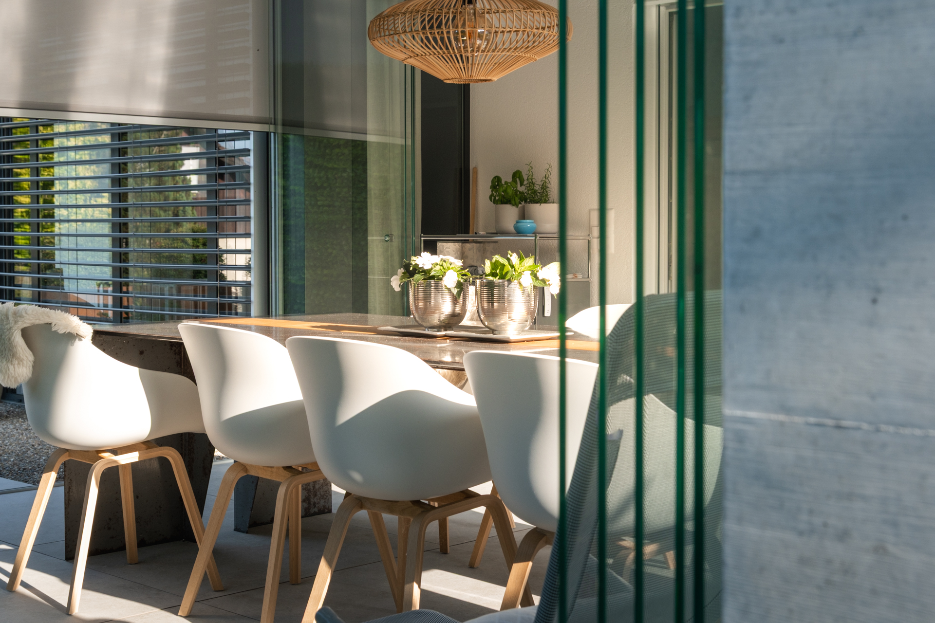 Weisse Gartenstühle an einem grossen Holztisch in der Loggia des Gartens. 