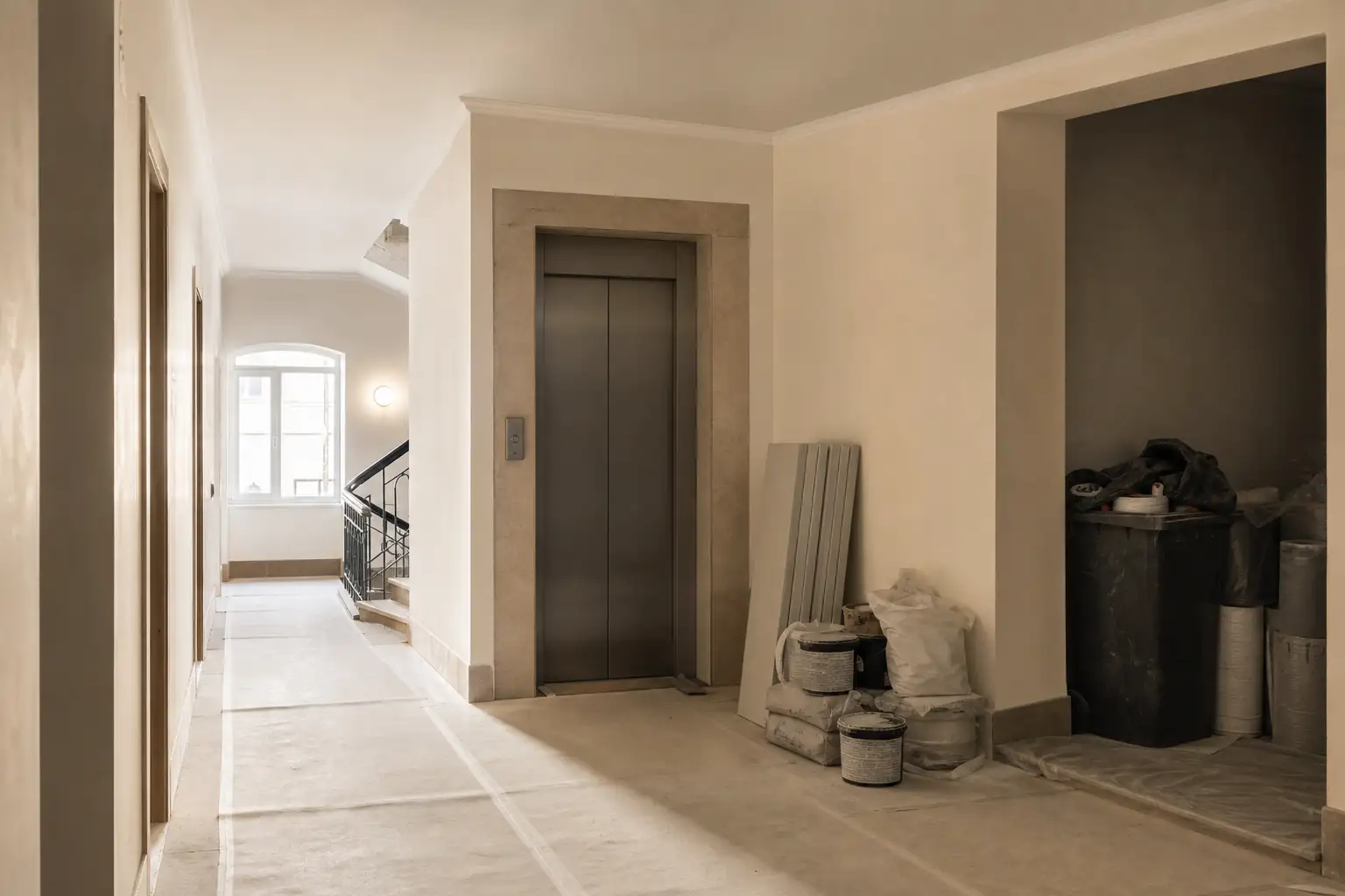 Corredor de prédio residencial preparado para trabalhos de remodelação, com proteções e materiais organizados.