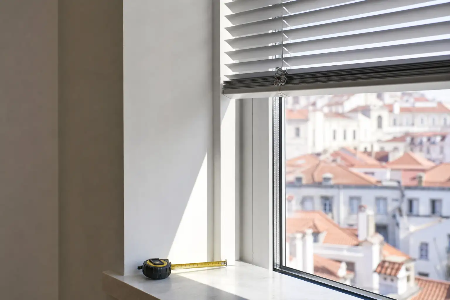 Pormenor de estore interior instalado num vão de janela de apartamento, com fita métrica sobre o peitoril.