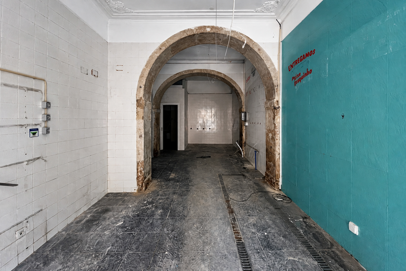 Antes: interior comercial em obra com arcos de pedra expostos, azulejos brancos e pavimento desmontado