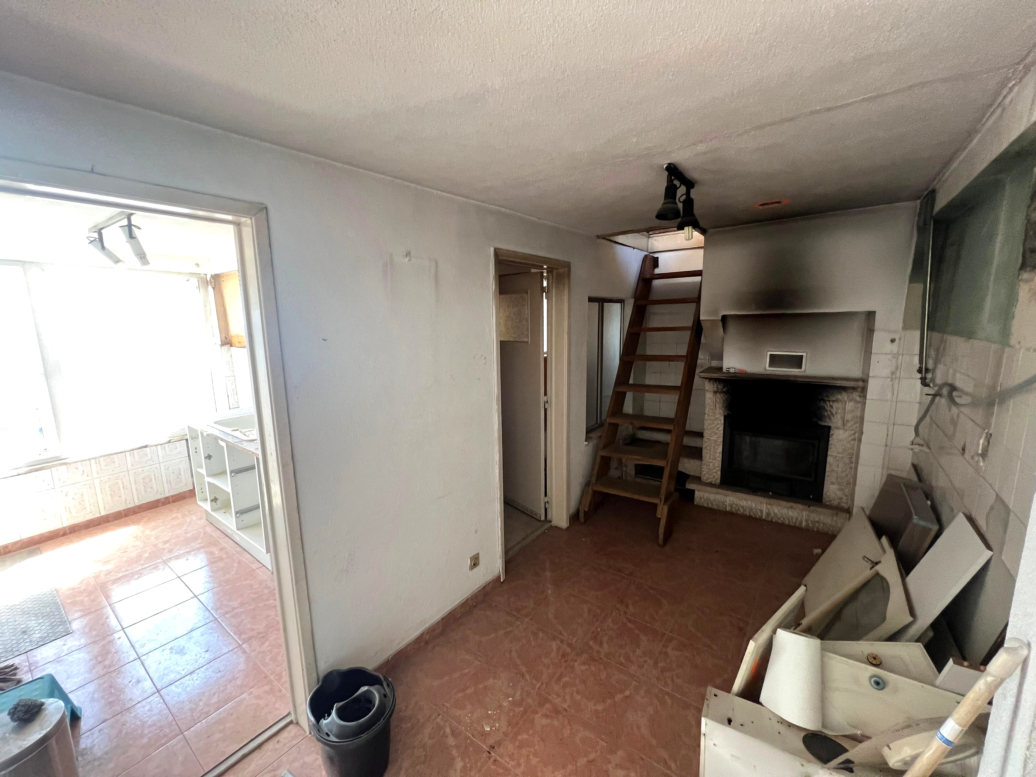 Antes: sala datada com escada de madeira, lareira revestida a pedra e cozinha ao fundo