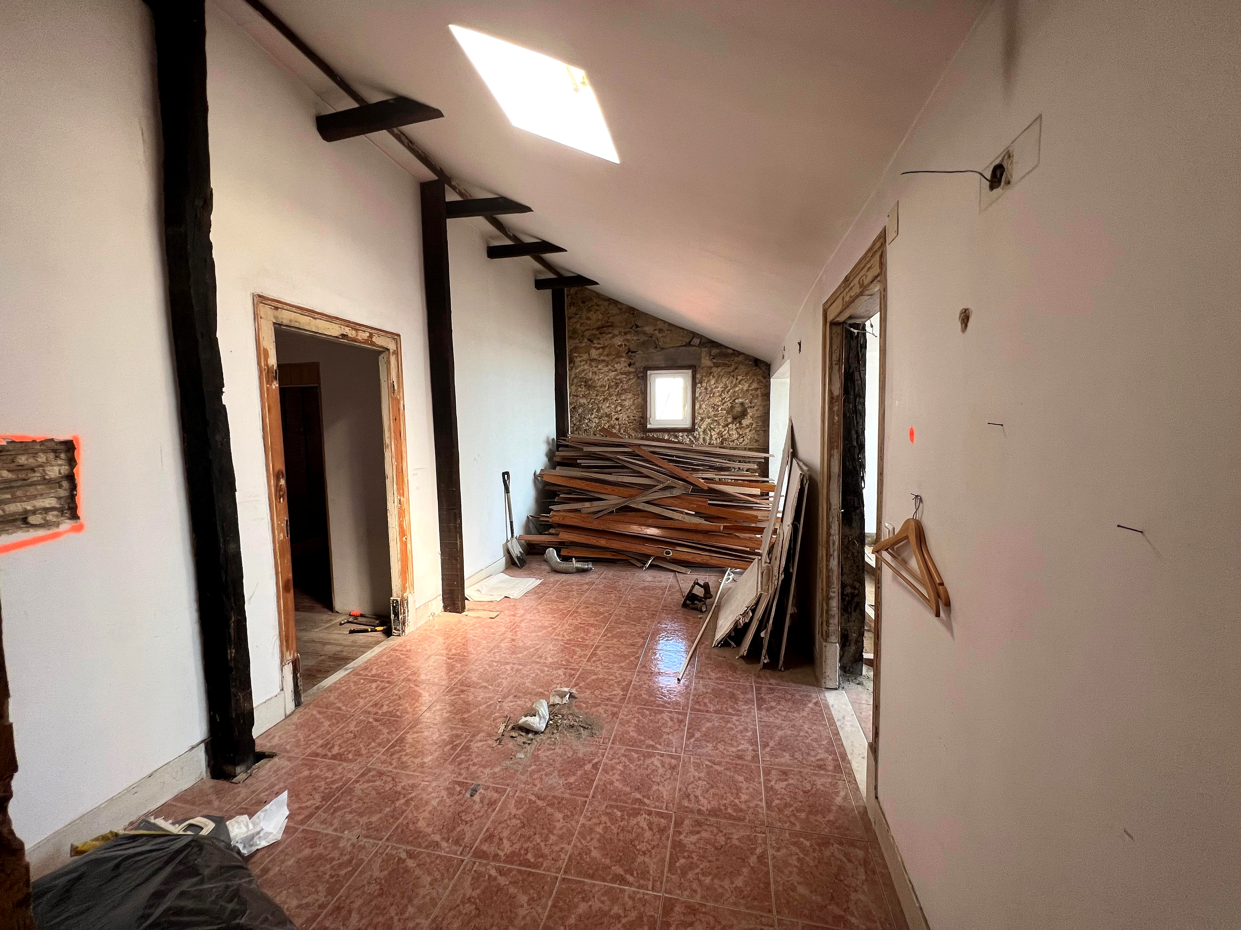 Antes: corredor em obra com parede de tijolo exposta, vigas escuras e materiais empilhados
