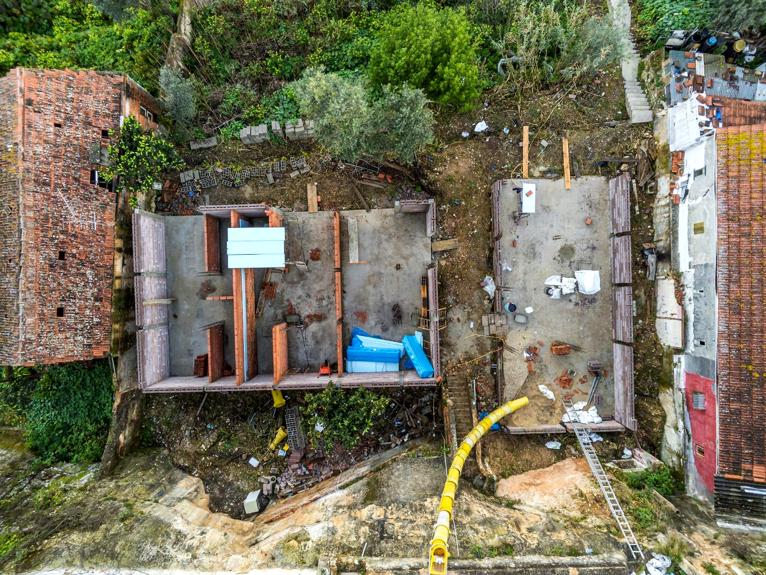 Antes: vista aérea de um pátio em obra, com pequenas coberturas, alvenaria e vegetação envolvente