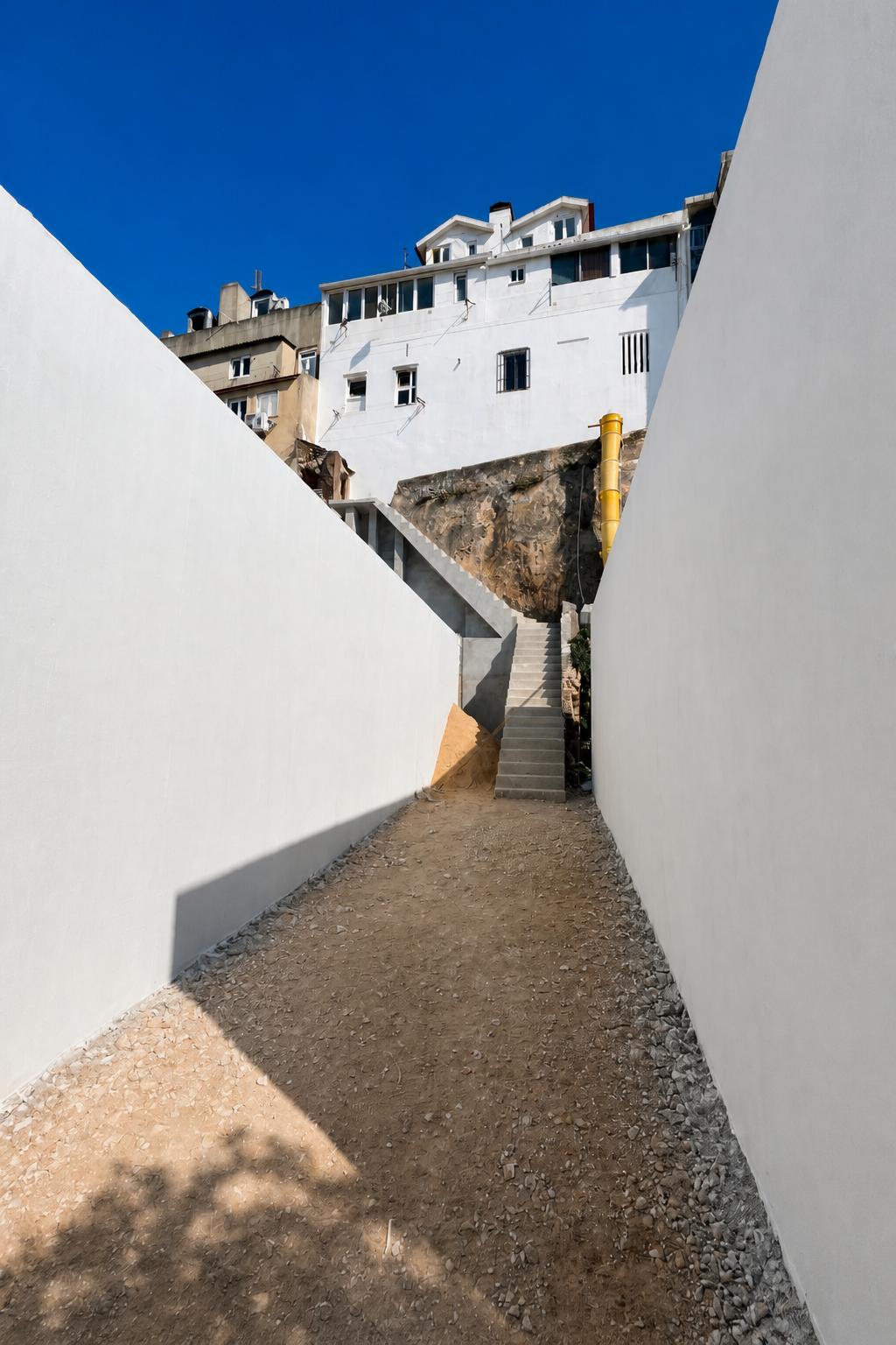 Depois: escada exterior reconstruída entre uma parede de blocos e a fachada, com tubagem amarela visível