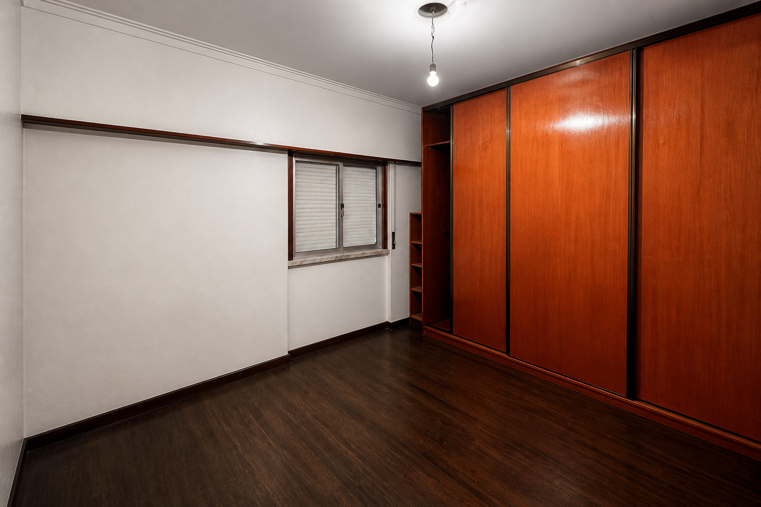 Antes: quarto com pavimento escuro, roupeiro em madeira de parede inteira e janela pequena