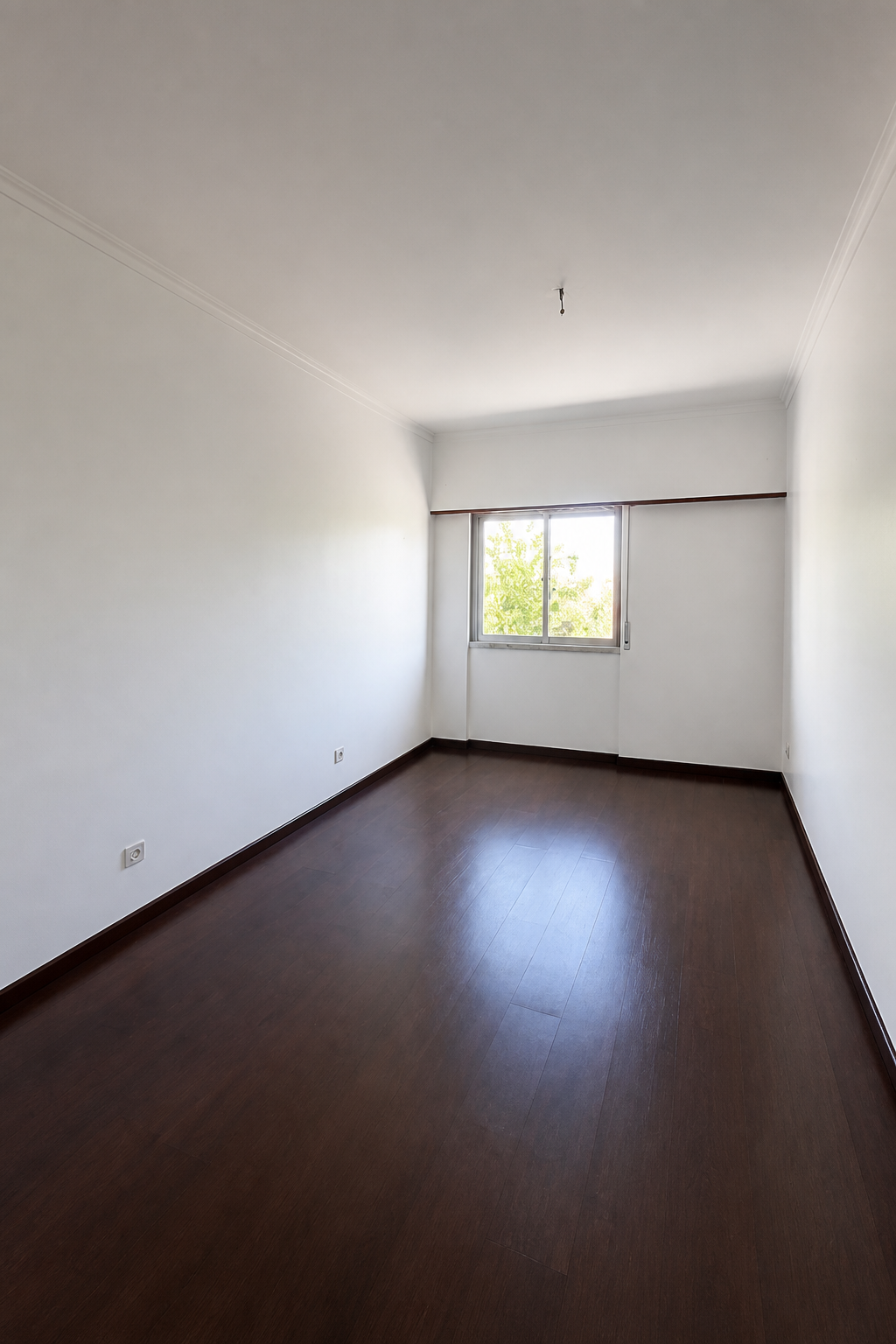Antes: quarto vazio com pavimento em madeira escura e janela lateral
