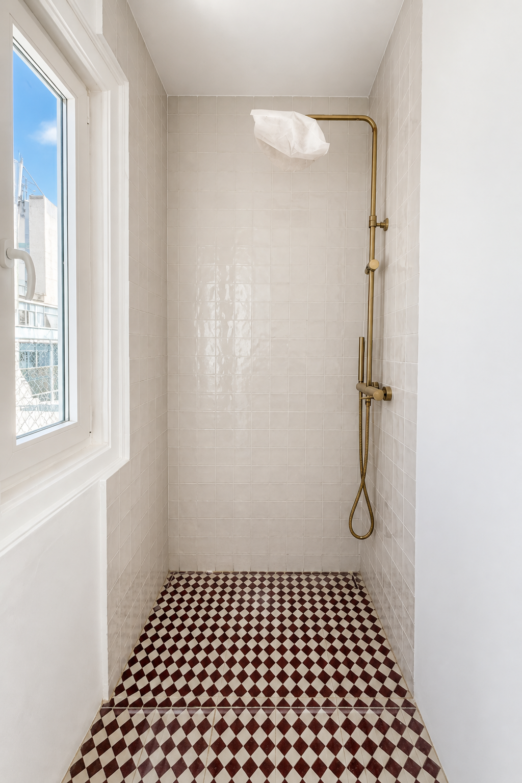 Depois: duche renovado com azulejos brancos, pavimento geométrico vermelho e torneiras em latão