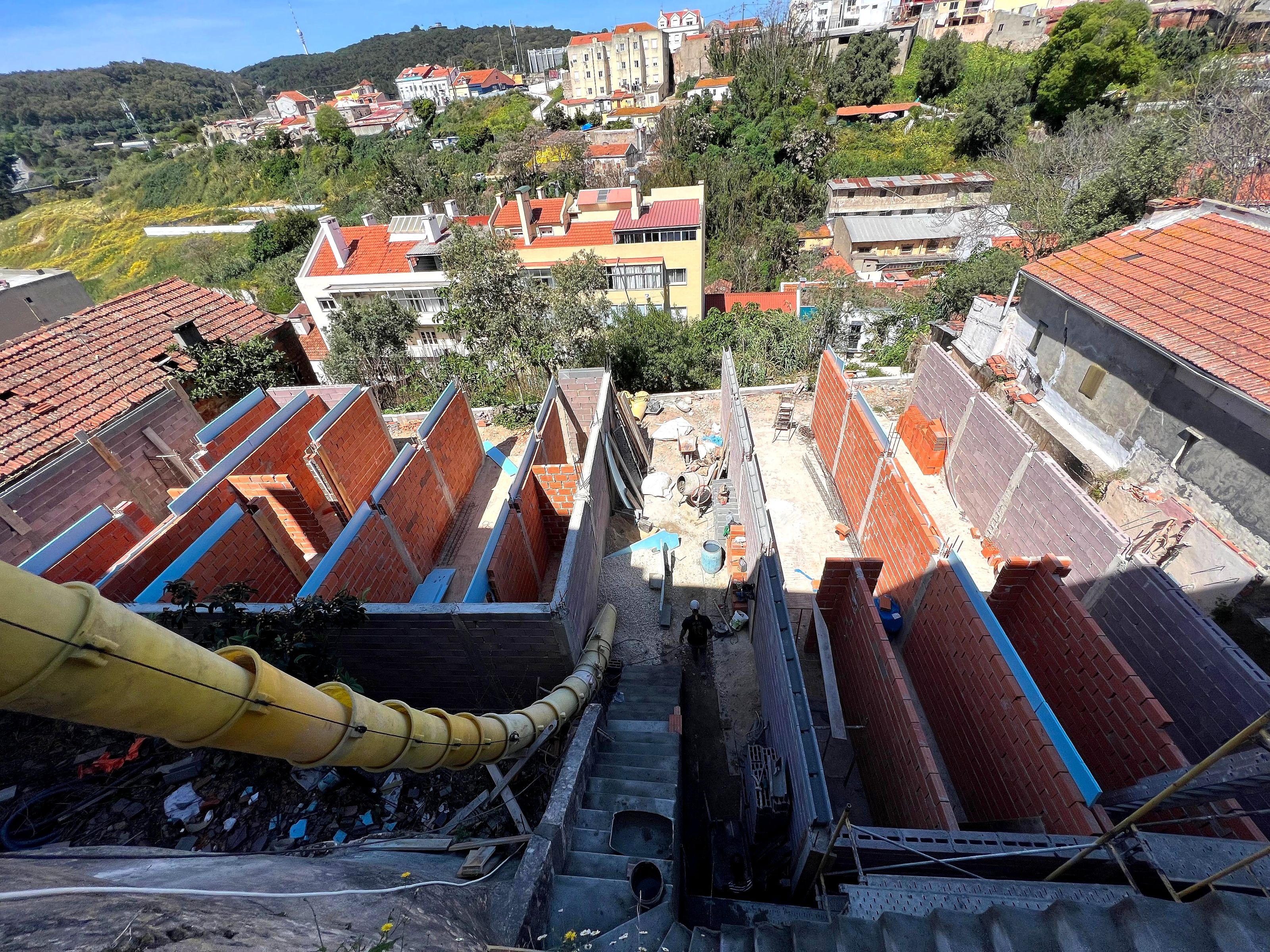 Antes: vista aérea sobre paredes de alvenaria recém-erguidas num lote inclinado