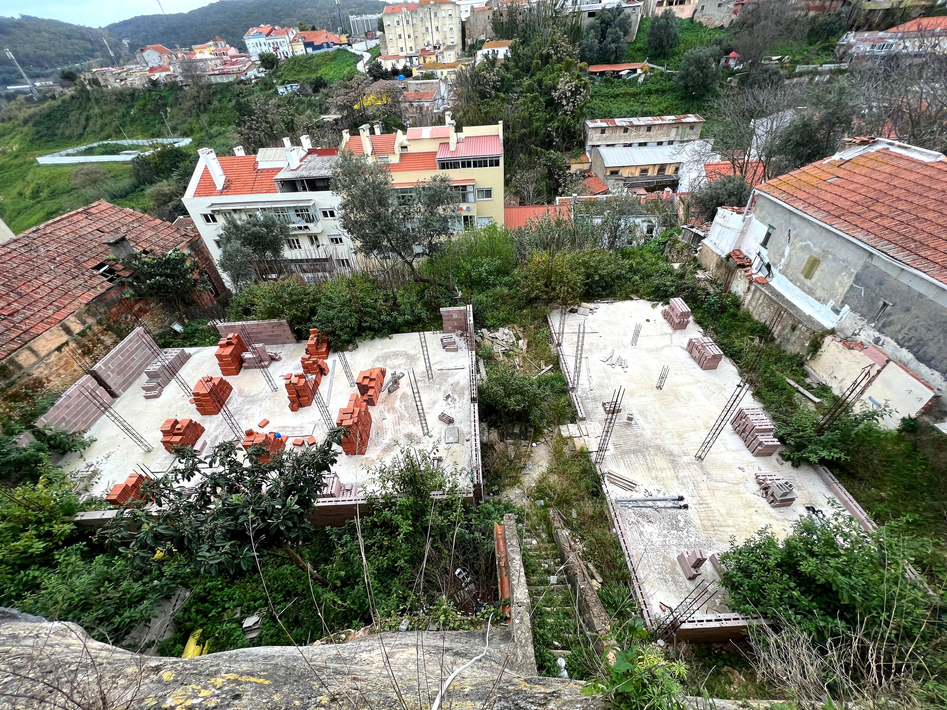 Antes: vista aérea de uma obra entre telhados, com paredes de alvenaria e terrenos envolventes