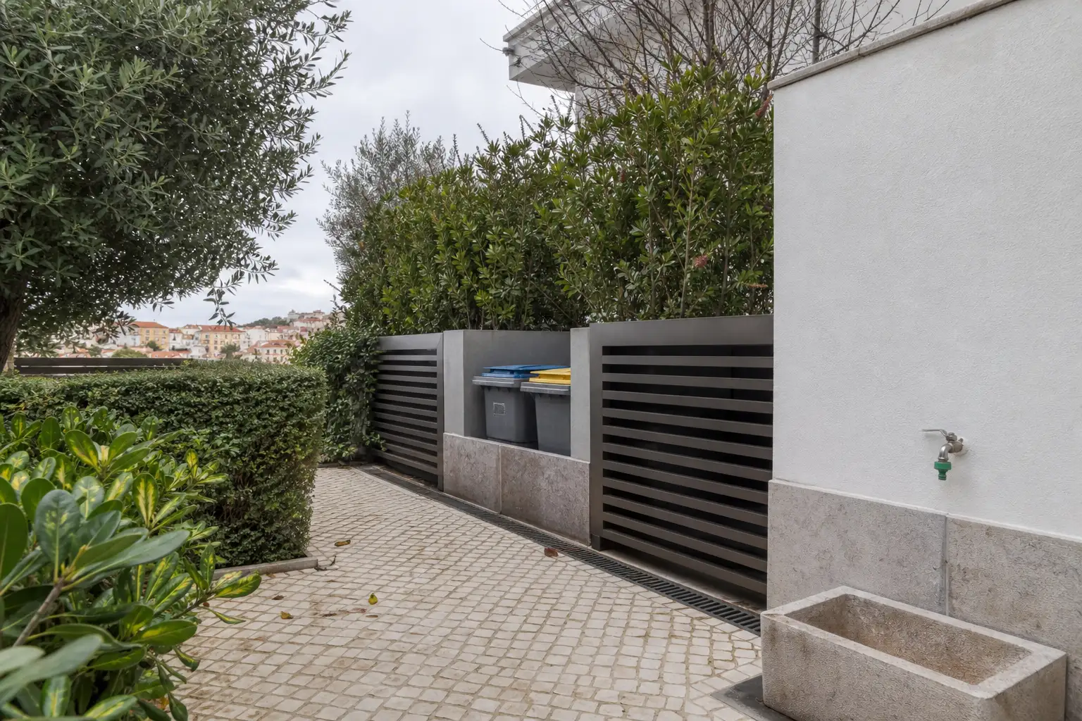 Garden service corner at a Lisbon house with bins behind slatted screening and a wash-down access route