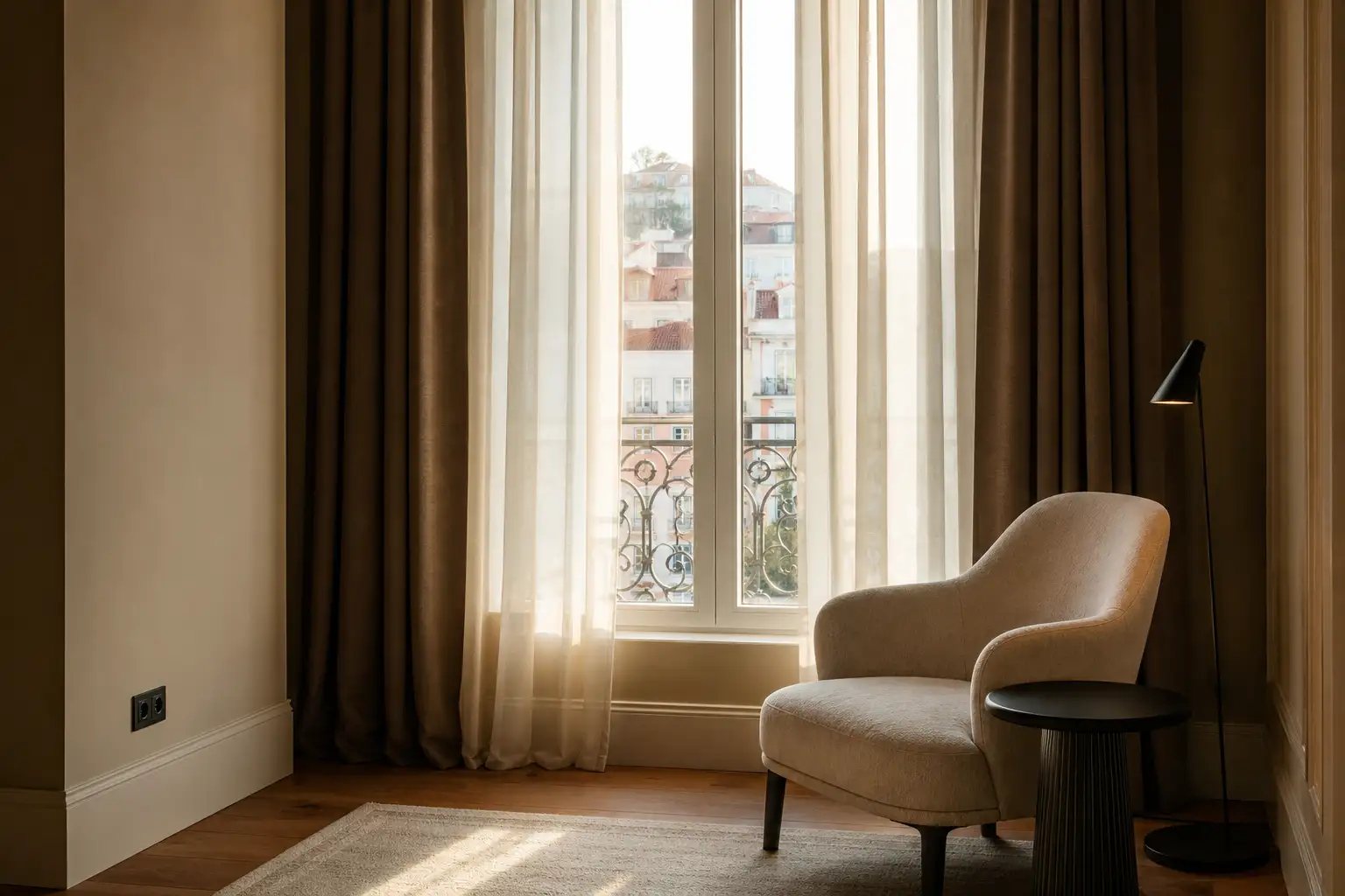 Pormenor de janela com cortinas em camadas e cadeira de leitura num interior residencial em Lisboa