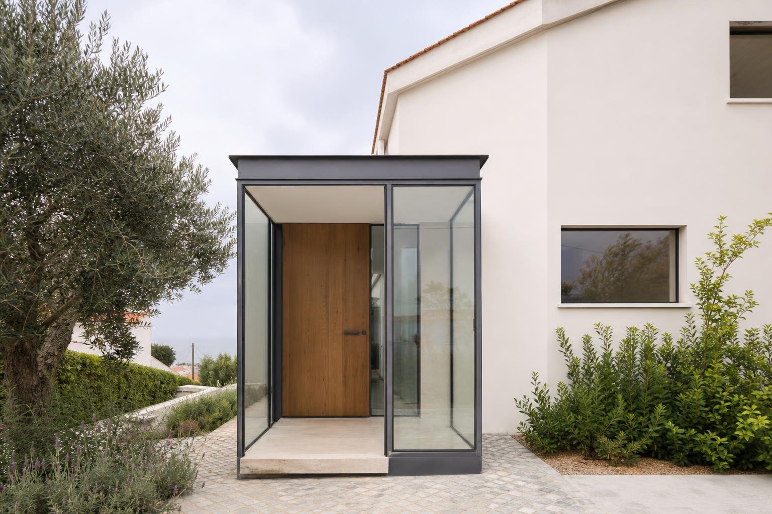 Entrada de moradia em Lisboa com vestíbulo corta-vento envidraçado, porta de madeira e cobertura discreta