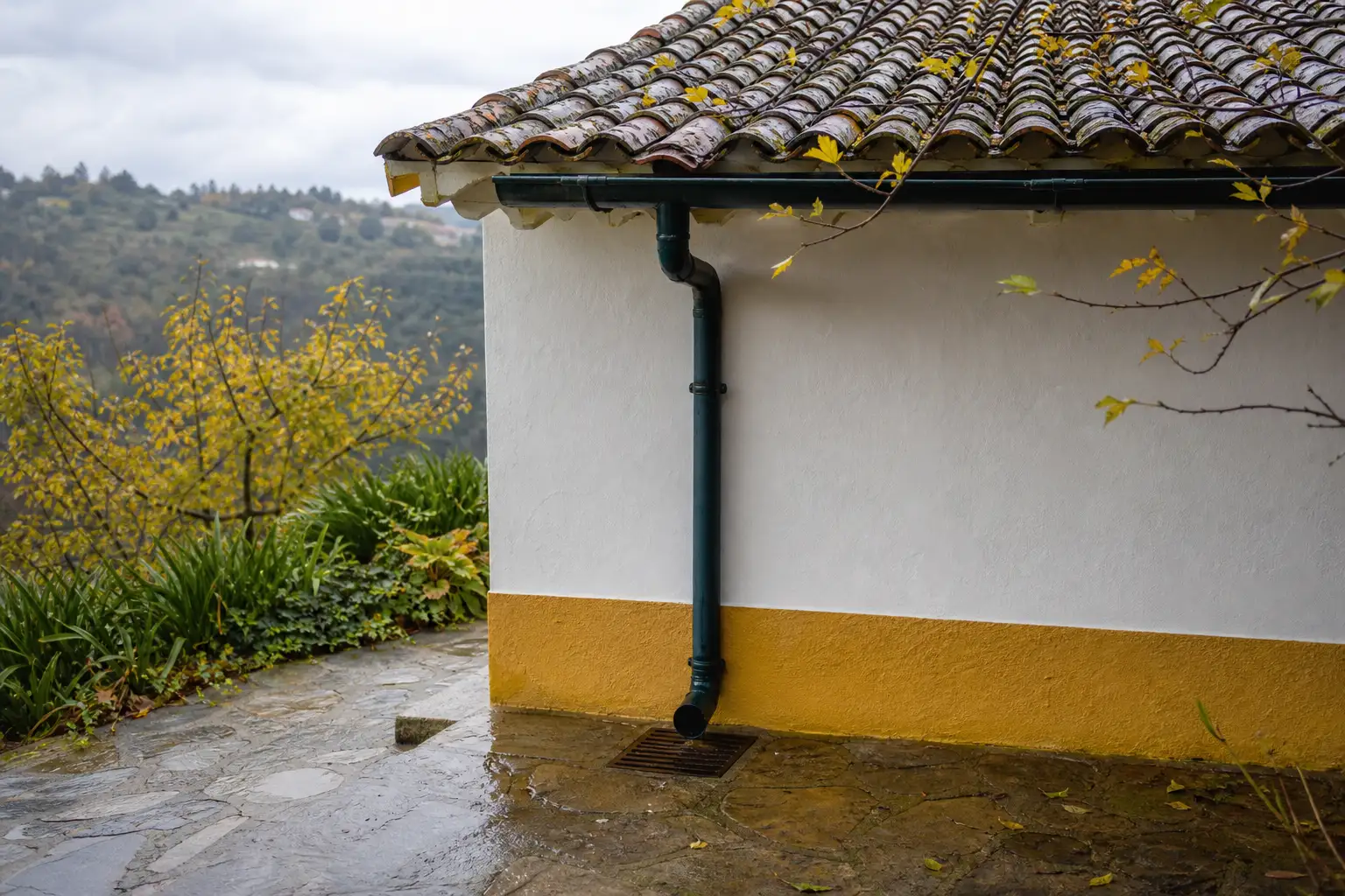 Close exterior view of a Portuguese house eave with roof tiles, gutter, downpipe and exterior drain.