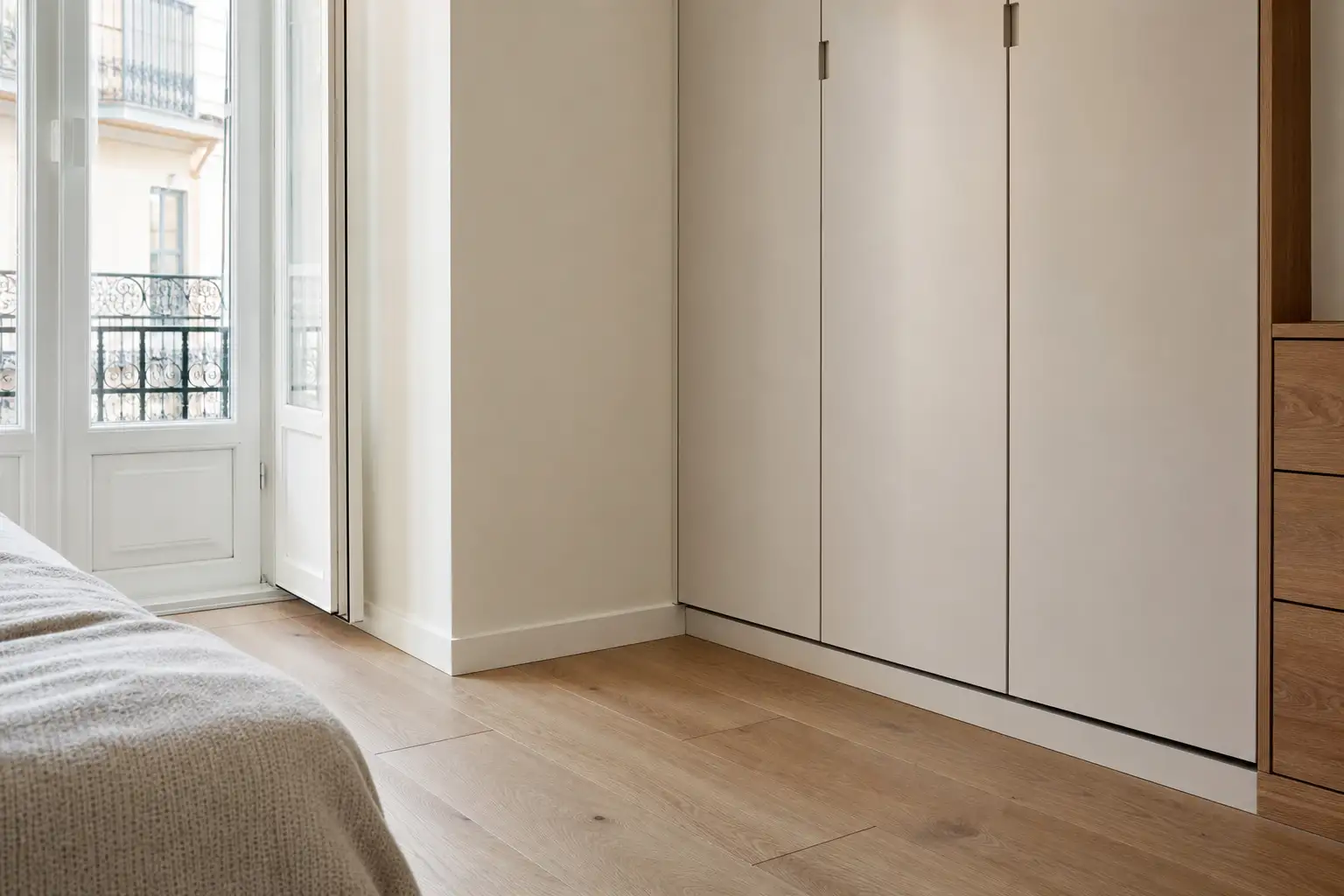 Pormenor de um quarto remodelado com pavimento de madeira, rodapé bem rematado e roupeiro ventilado.