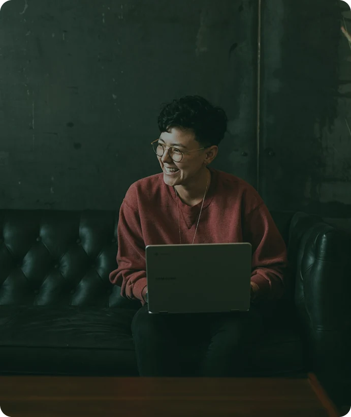 Smilende medarbejder med en laptop i en sofa.
