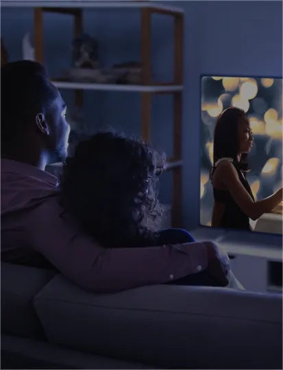 A man and woman sitting together on a couch, watching television.