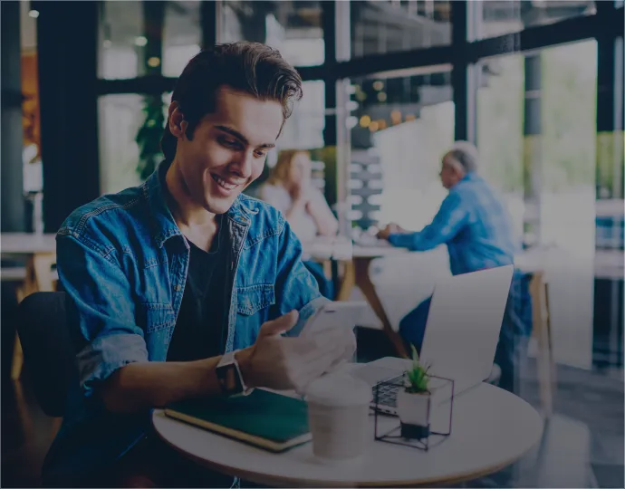 A man enjoying a cup of coffee at a table, smiling and using his mobile phone.