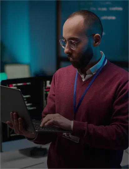 A man wearing glasses is focused on his laptop, concentrating on the screen.