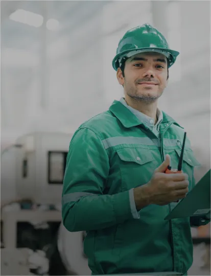 A man wearing a green uniform and a construction helmet is holding clipboard and shortwave radio.