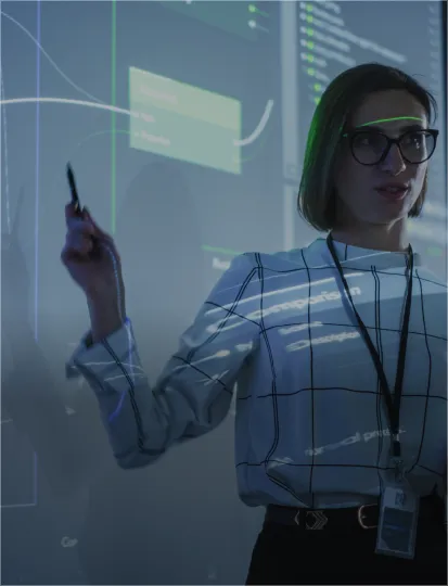 A woman in glasses gestures towards a whiteboard with information shown from a multimedia projector.