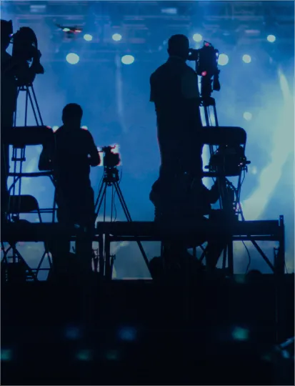 Technicians' silhouettes on stage, equipped with cameras, documenting the event.