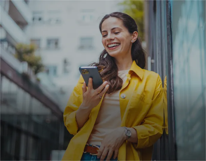 A woman in a yellow shirt smiles while holding a cell phone.