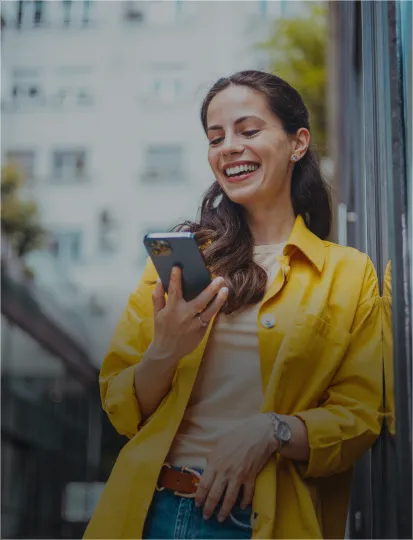 A woman in a yellow shirt smiles while holding a cell phone.