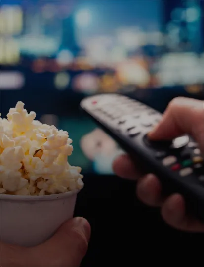 A person with a bowl of popcorn and a remote control, preparing to watch tv.