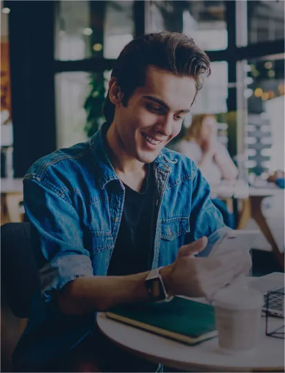 A man enjoying a cup of coffee at a table, smiling and using his mobile phone.