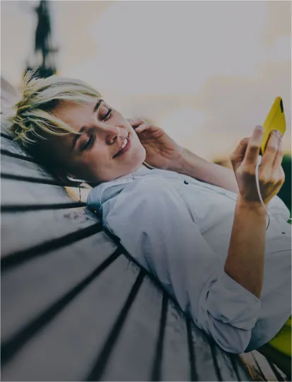 A woman lies on a bench outdoors, holding a mobile phone in her hand.