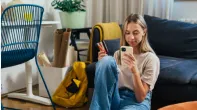 A woman sitting on the floor, holding her phone and credit card, engaged in digital banking activities.