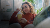 Young woman sitting on a couch, smiling as she looks at her smartphone, illustrating positive customer engagement in the era of AI.