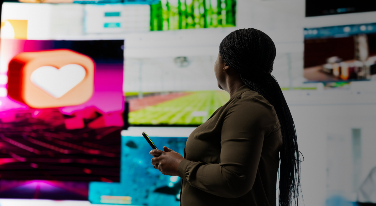A woman poses in front of a large screen filled with multiple diverse images. 
