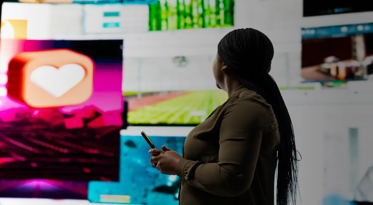 A woman poses in front of a large screen filled with multiple diverse images.