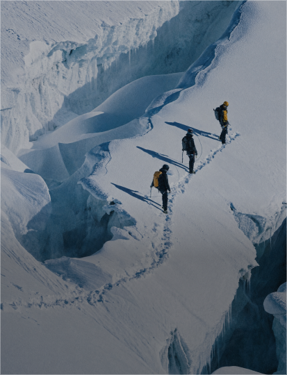 Three people trekking on a mountain side, with a panoramic view of the landscape around them.