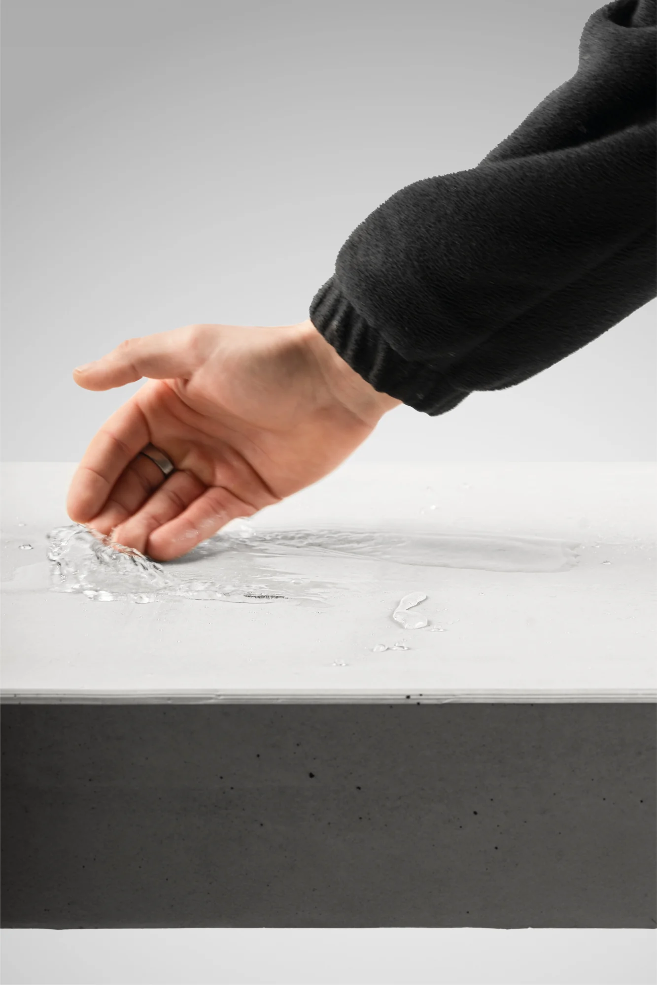Eine Hand wischt Wasser über die Oberfläche eines Betonmöbels.
