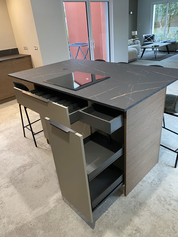 Détail de l’îlot central avec tiroirs ouverts, rangements optimisés et plan de travail sombre au veinage continu.