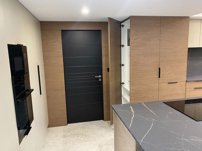 Porte intégrée dans une façade bois, cuisine sur mesure avec rangements dissimulés et colonnes de rangement.