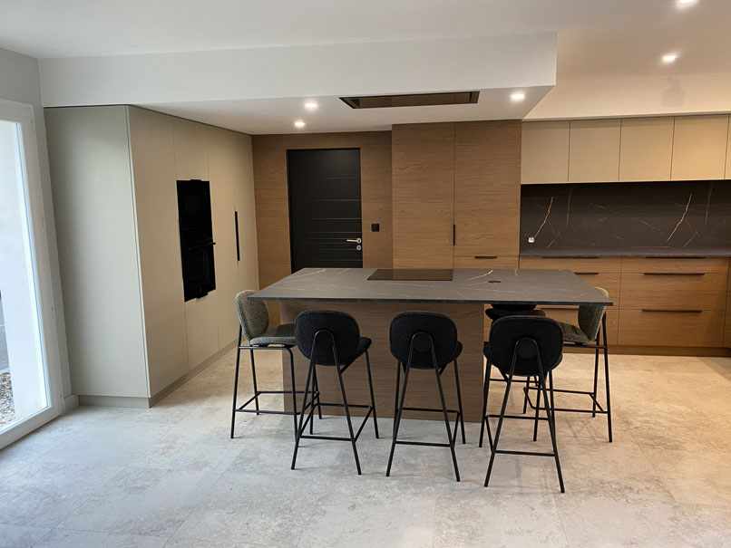 Cuisine moderne sur mesure avec îlot central en stratifié effet marbre sombre, façades bois et rangements intégrés, vue générale de la pièce de vie ouverte.