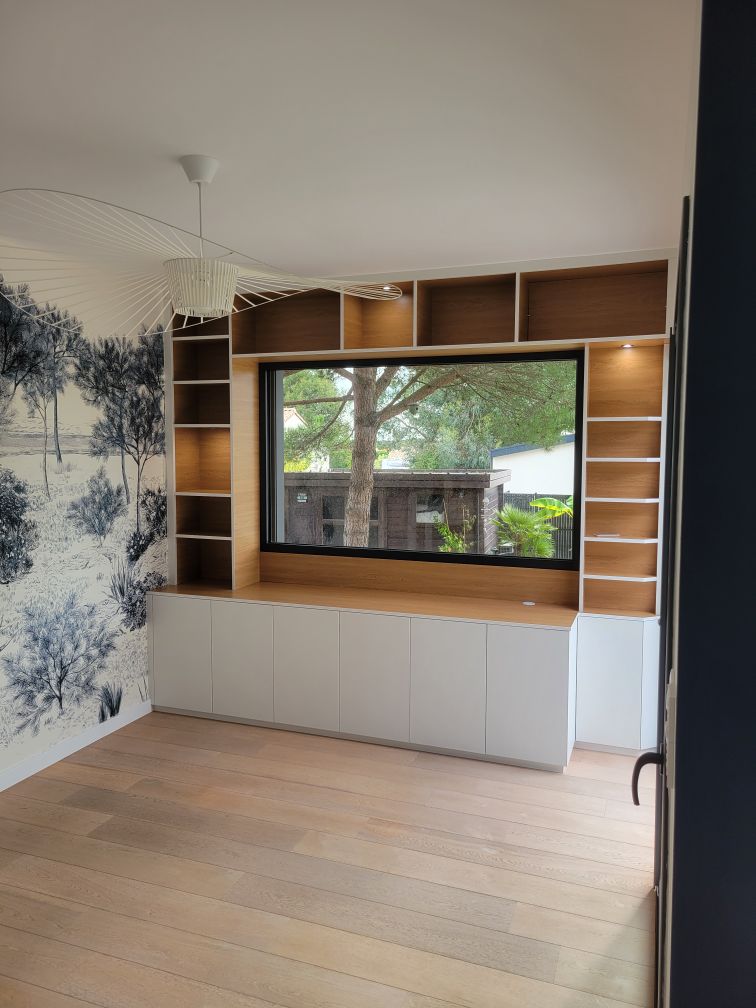 Bibliothèque sur mesure en bois clair et blanc, intégrée à une baie vitrée avec finitions soignées