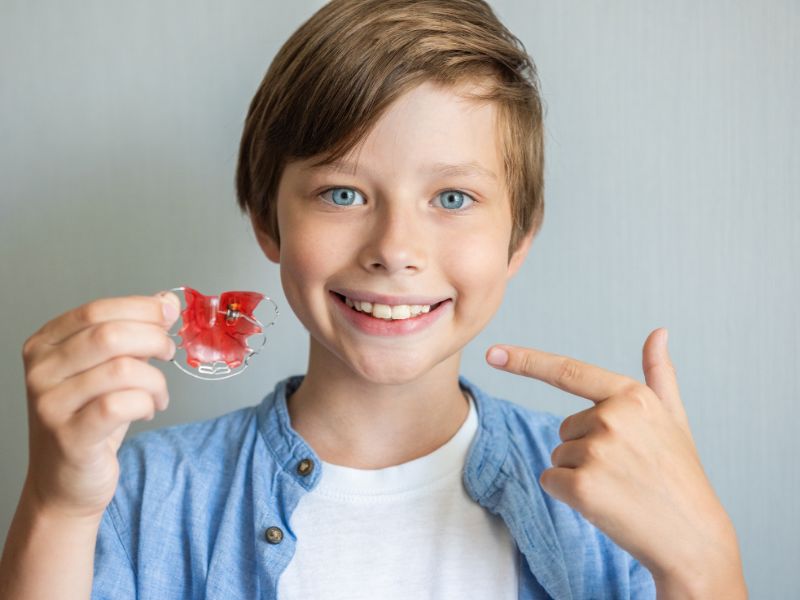 Child holding and pointing to his custom orthodontic retainer